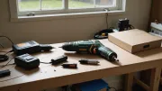 Perceuse-visseuse sans fil posée sur un établi en bois brut, à côté de deux batteries et d'un chargeur, sous une lumière d'atelier