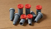 Chevilles en plastique gris à collerette rouge, les unes nervurées et droites, les autres coniques, posées debout et couchées sur un plan de travail en bois clair