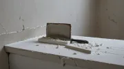 Couteau à enduire chargé d'enduit blanc devant un mur clair présentant un trou, bâche de protection posée au sol